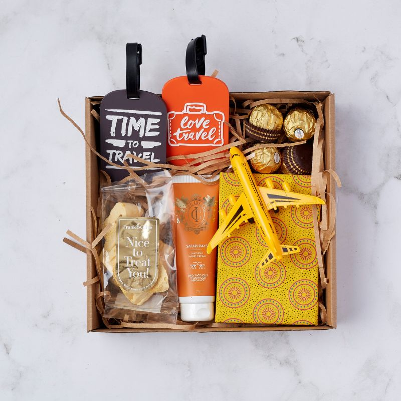 Travel-themed gift box with luggage tags, airplane toy, hand cream, snacks, and chocolates.