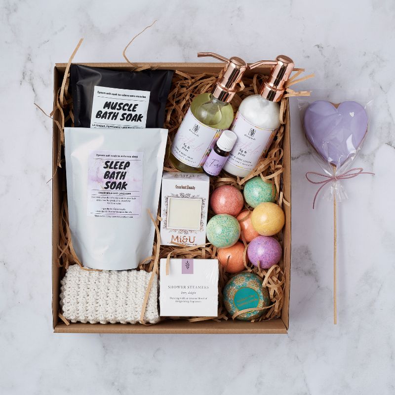 Luxury pamper gift box featuring muscle bath soak, sleep bath soak, hand and body wash, bath bombs, and a heart-shaped lollipop.