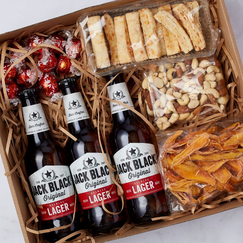 Gift box with three Jack Black Lager beers, mixed nuts, dried mango, cheese sticks, and Lindt chocolates in eco-friendly packaging.