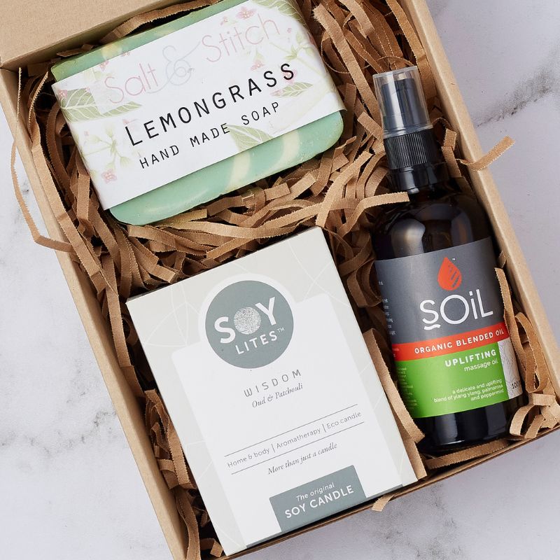 Close-up of a wellness gift box featuring a lemongrass soap bar, oud and patchouli soy candle, and organic blended massage oil.