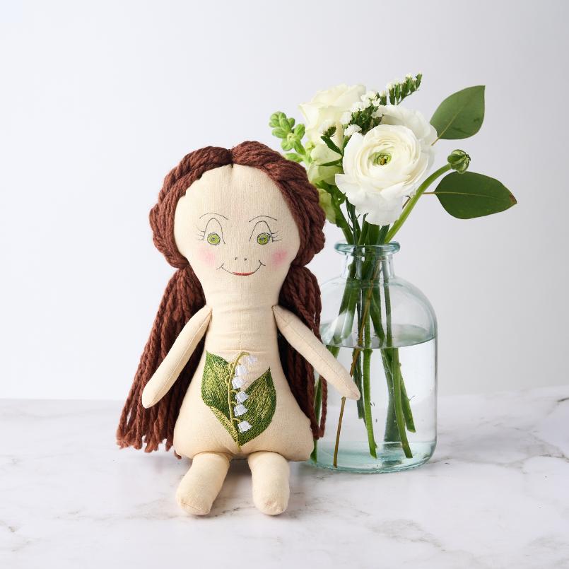 Lily of the Valley Doll sitting next to a glass vase with white flowers, featuring hand-embroidered details and brown yarn hair.