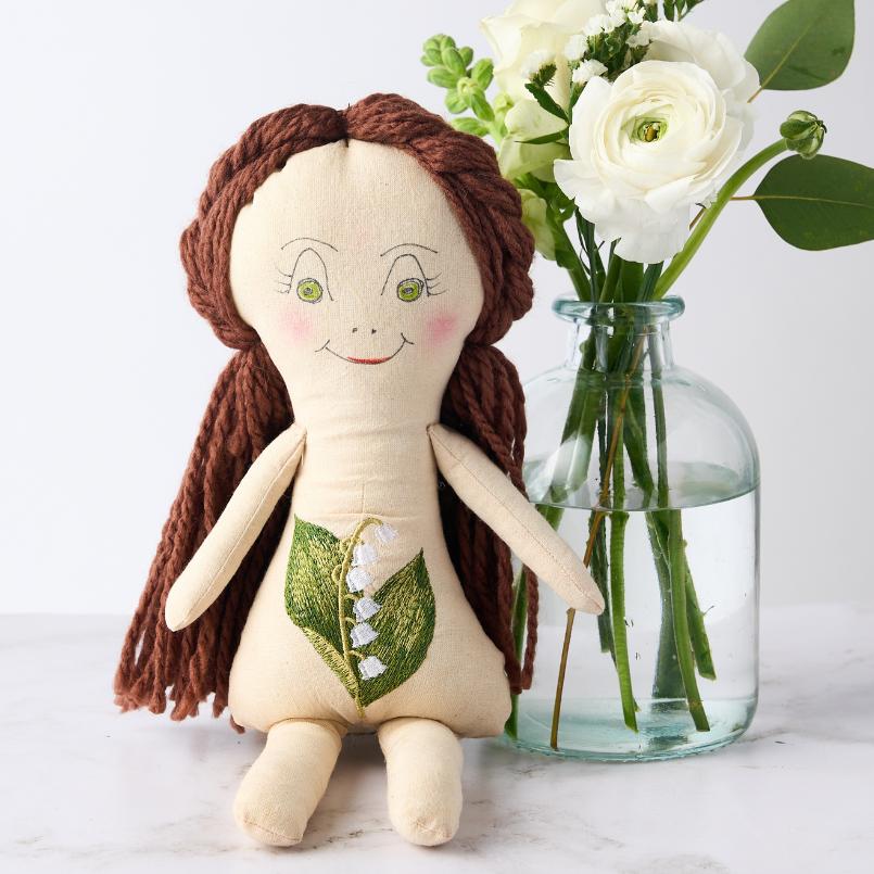 Lily of the Valley Doll with a green leaf and lily of the valley embroidery, posed with a bouquet of white flowers in a vase.