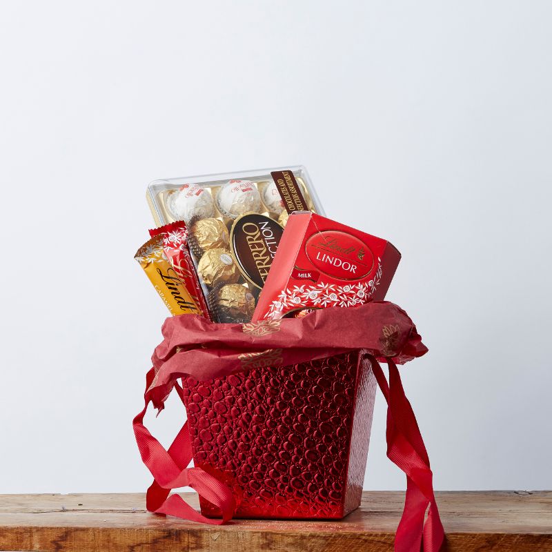 Lindt Vs Ferrero gift basket featuring Ferrero Rocher chocolates, Lindt Lindor milk chocolate, and other premium chocolate treats in a red decorative basket.