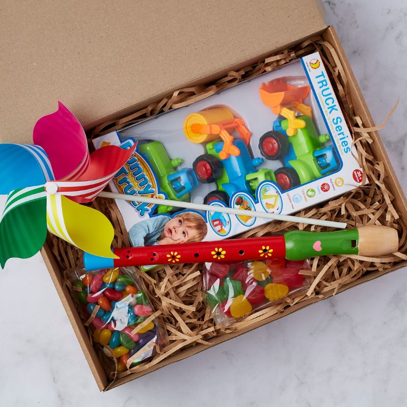 Kids' gift box featuring a toy truck set, colourful pinwheel, wooden flute, and assorted sweets in a gift-ready box.