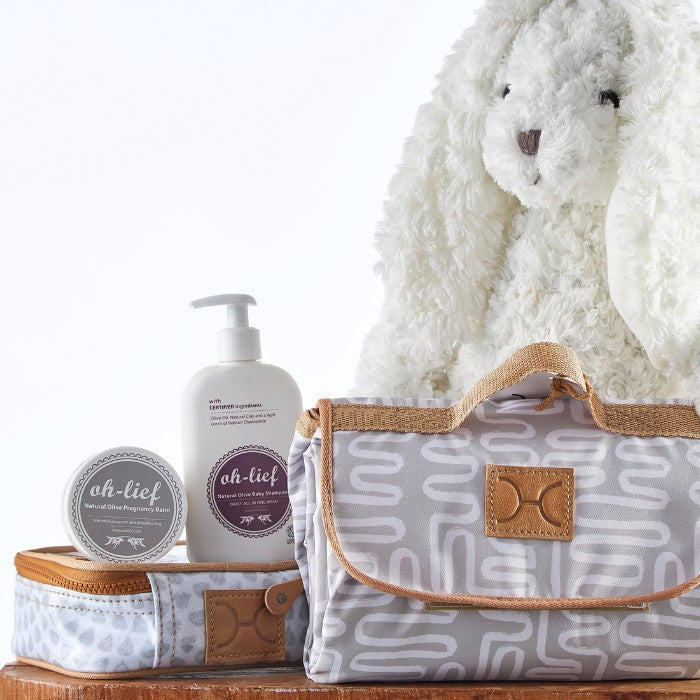 Elegant baby gift set with a soft white rabbit toy, natural olive baby shampoo, and a chic patterned carry bag.