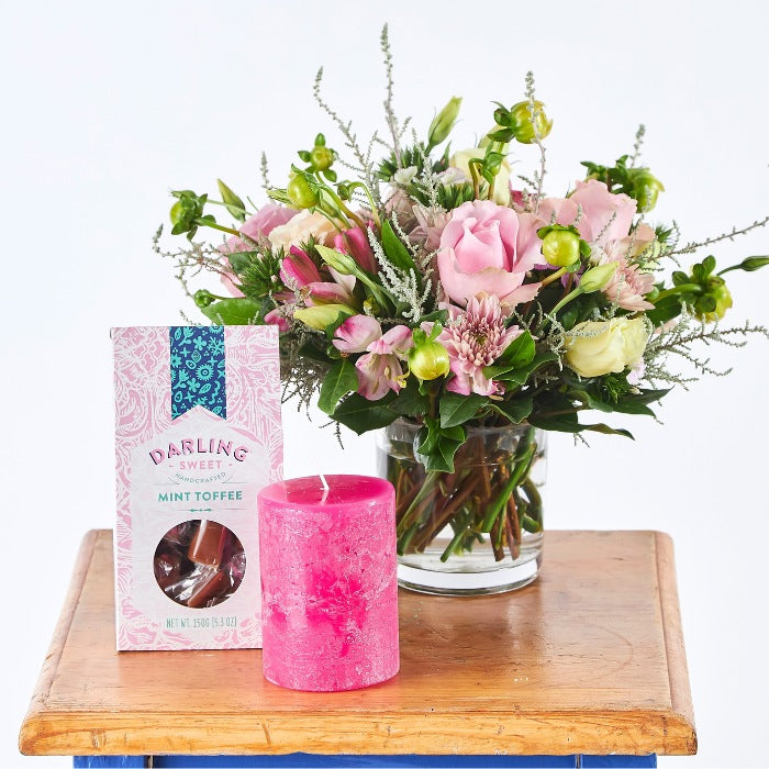 Elegant flower arrangement from the Love and Light Gift Set, paired with a pink candle and mint toffee, presented on a wooden table for a delicate touch.