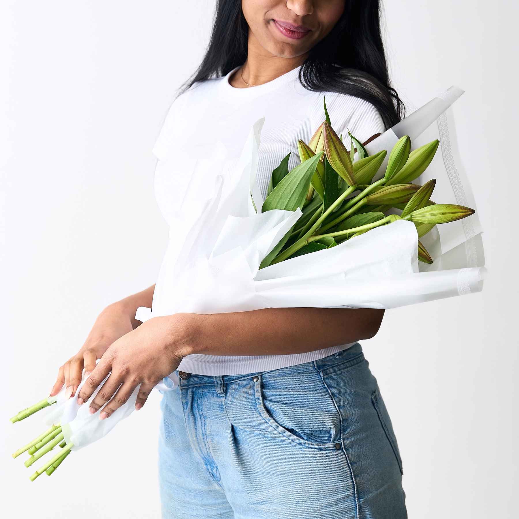 A woman holding a simple and elegant bouquet of unopened lilies wrapped in white paper, highlighting the fresh and natural beauty of the flowers.