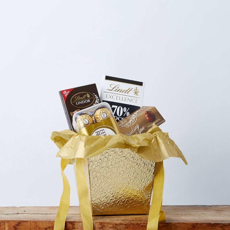 Golden gift basket filled with Lindt chocolates, Ferrero Rocher, and 70% dark chocolate bar, wrapped in elegant yellow tissue.