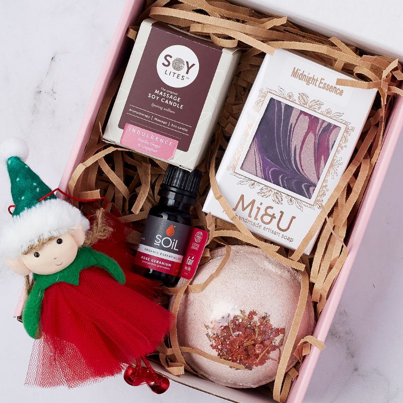 Festive gift box with a SoyLites massage soy candle, Mi&U handmade artisan soap, SOiL rose geranium essential oil, bath bomb, and a decorative Christmas elf doll.