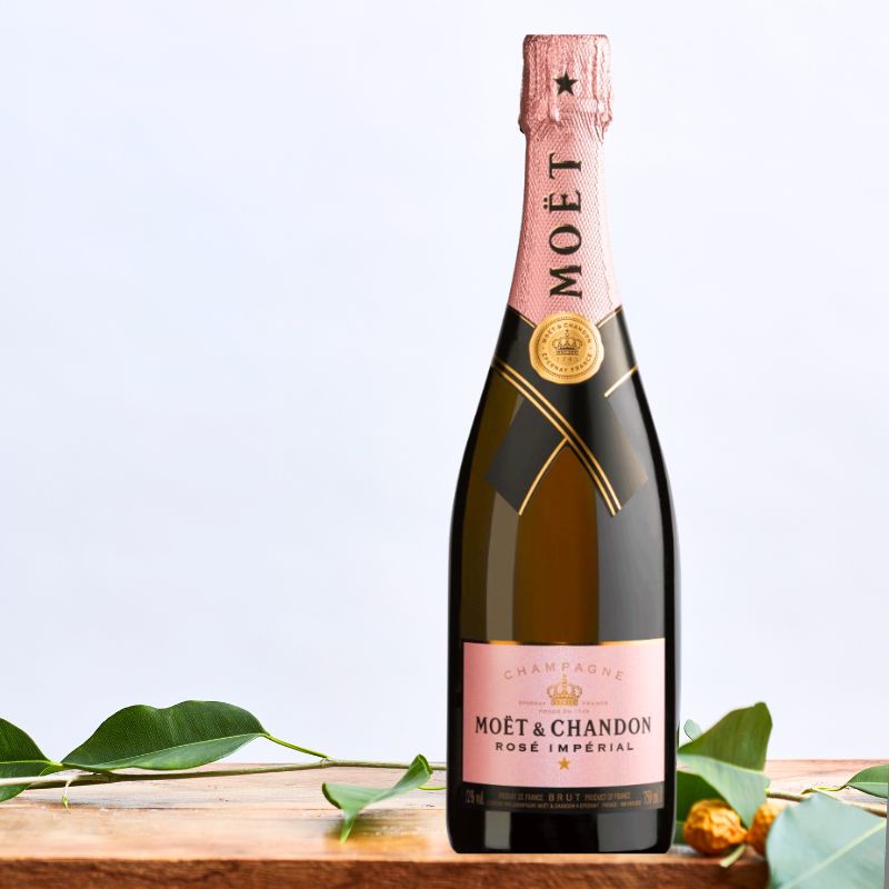 Moët & Chandon Rosé Impérial champagne bottle with elegant pink accents displayed on a wooden table with green foliage.