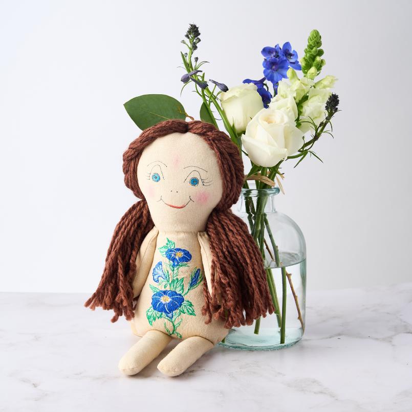 Morning Glory Dreams Doll with blue morning glory embroidery, paired with a vase of white and blue flowers.