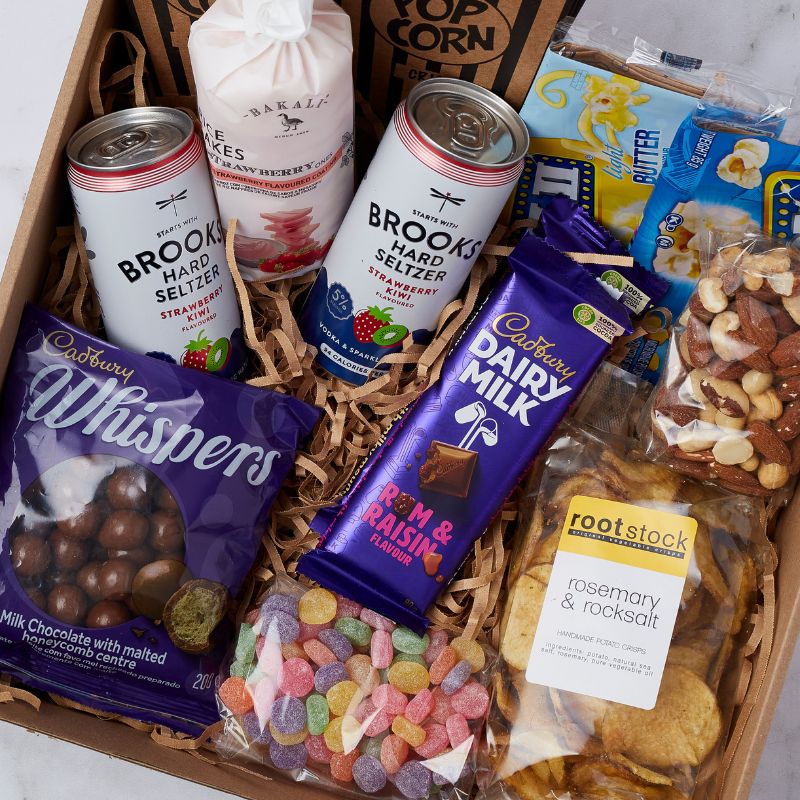 Close-up view of a Movie Night Box featuring assorted snacks including Brooks Hard Seltzer cans, Cadbury chocolate bars, Whispers chocolates, gummy sweets, mixed nuts, and Rootstock rosemary & rock salt chips.