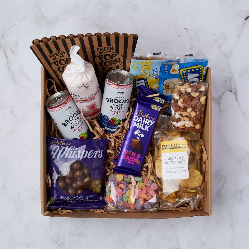 Movie Night Box filled with a variety of snacks such as popcorn, Brooks Hard Seltzer cans, Cadbury chocolate bars, Whispers chocolates, mixed nuts, and Rootstock chips, arranged in a gift box.