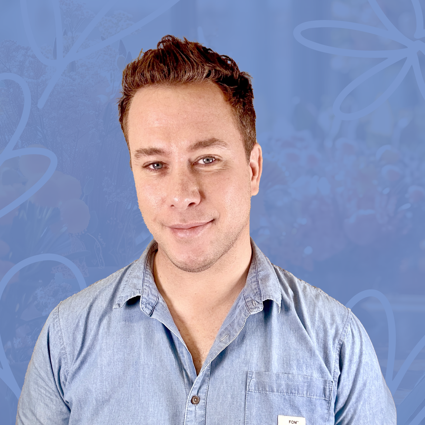 Portrait of Nicholas James, team member at Fabulous Flowers, smiling in a light blue button-up shirt against a blue background with floral designs. MEET THE TEAM at Fabulous Flowers and Gifts. Connect with Nicholas for expert floral and gift advice.