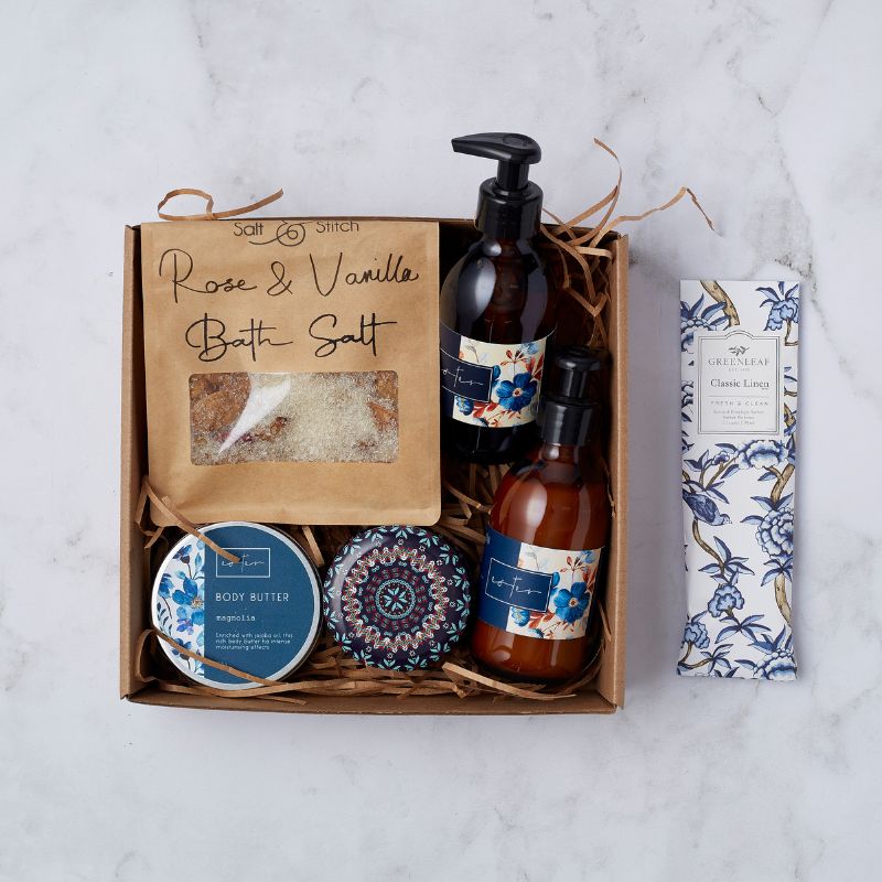 Opulent Oasis gift set featuring rose and vanilla bath salt, body butter, magnolia-scented hand and body wash, and a classic linen sachet.