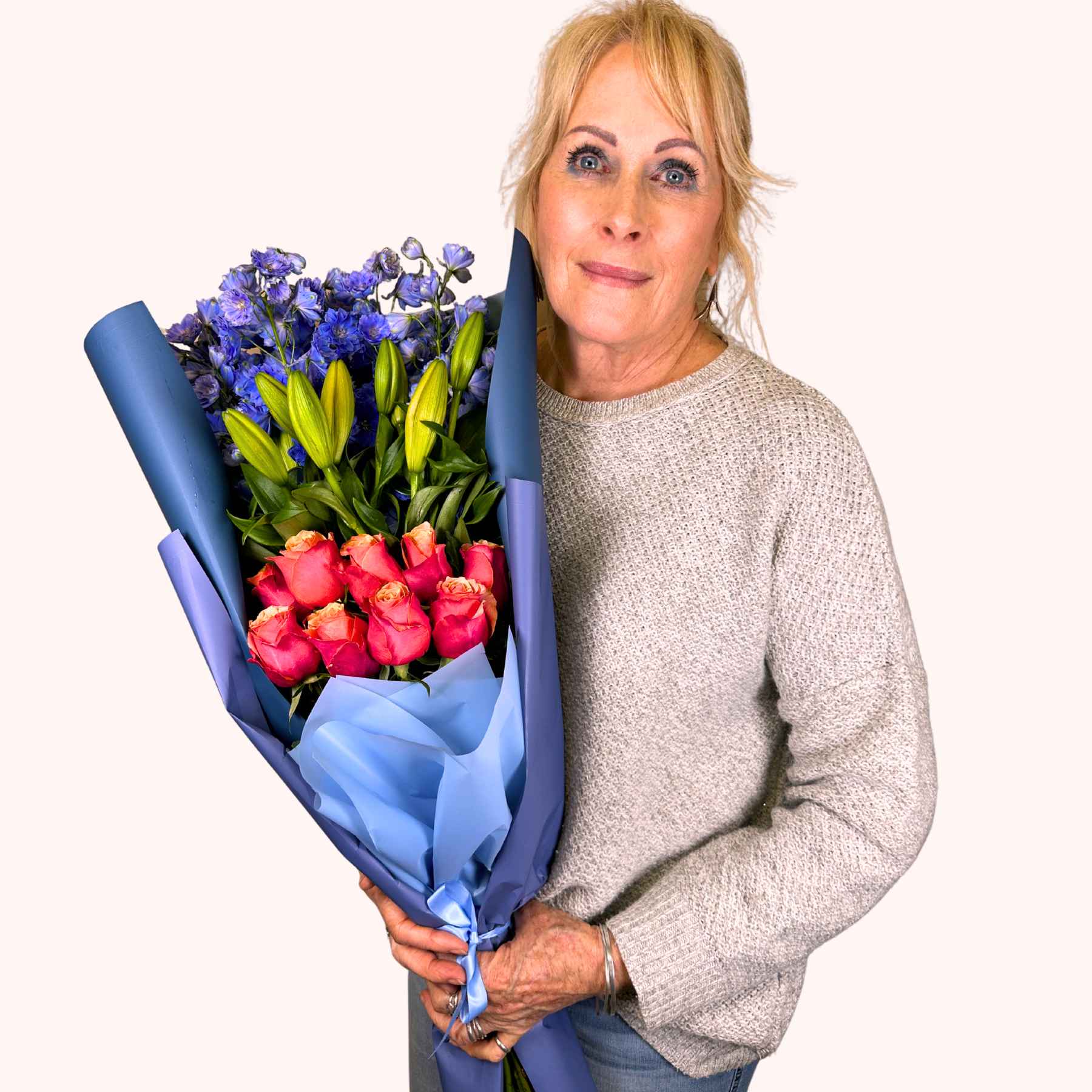 Woman holding an Orange Blue Bloom Bouquet with orange roses, lilies, and blue delphiniums, presented by Fabulous Flowers and Gifts.