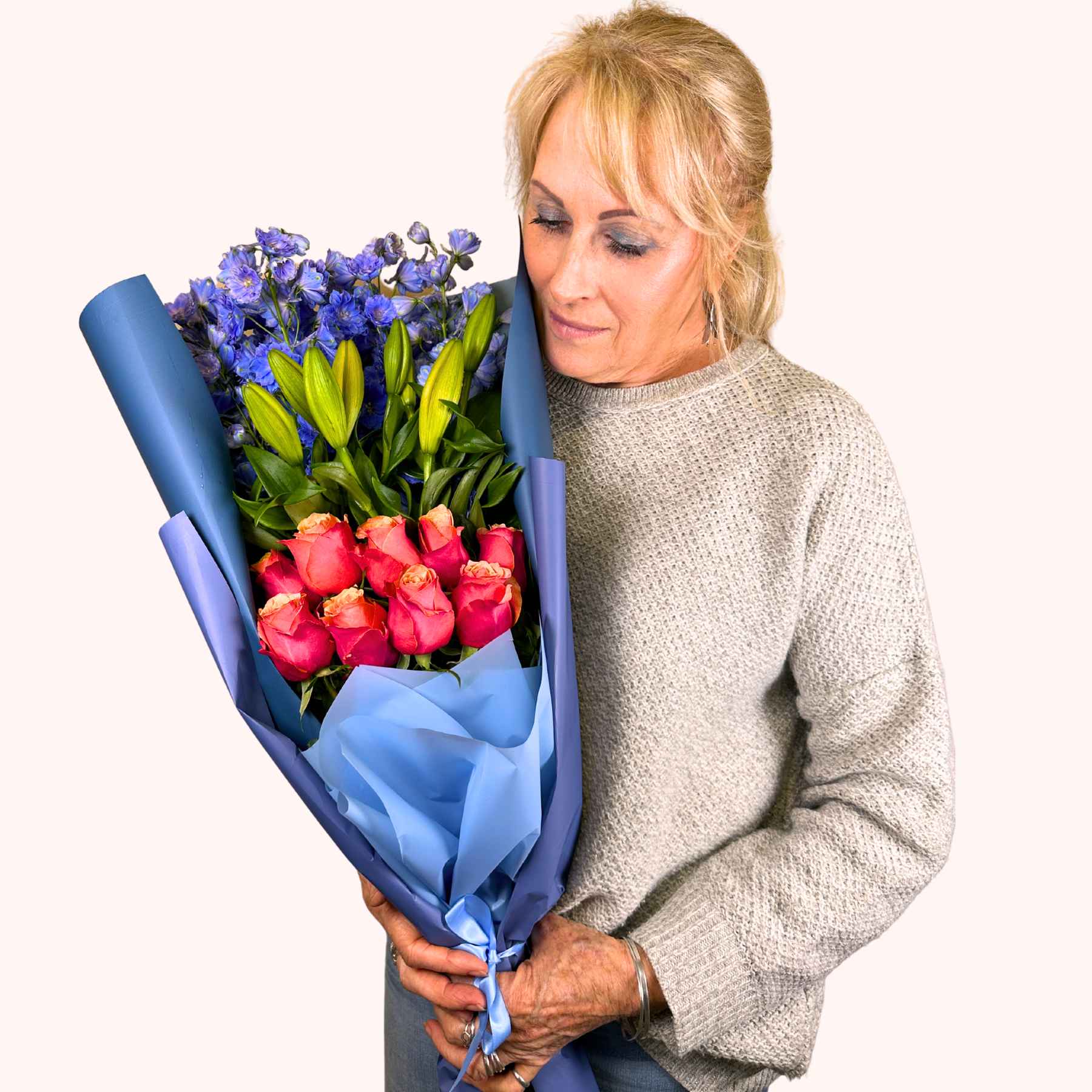 Woman looking at an Orange Blue Bloom Bouquet with orange roses, lilies, and blue delphiniums, presented by Fabulous Flowers and Gifts.