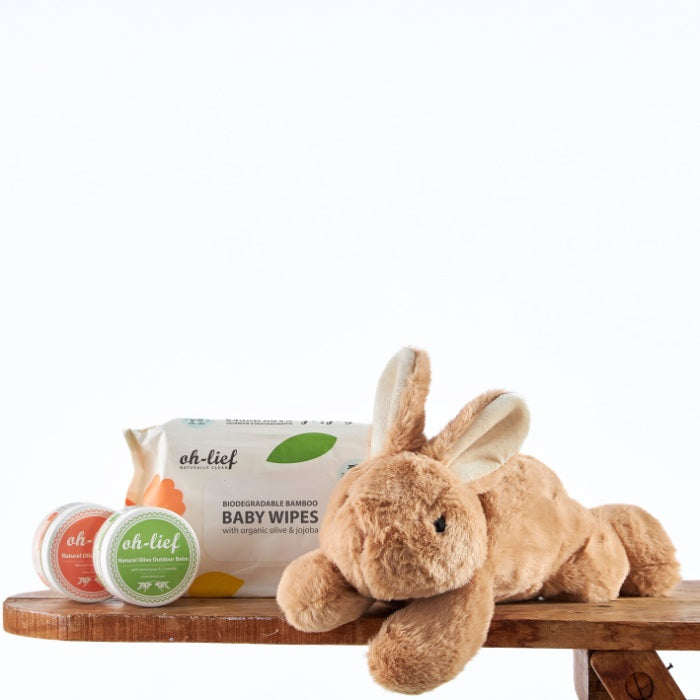 Organic Hopper Baby Essentials featuring a plush brown bunny, biodegradable bamboo baby wipes, and natural skin balms on a wooden surface, ideal for gentle baby care.