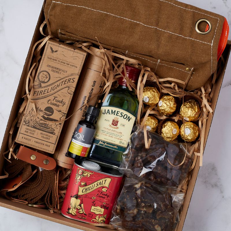 Close-up of Outdoor Adventure gift box contents, featuring whiskey, firelighters, chili salt, and gourmet treats