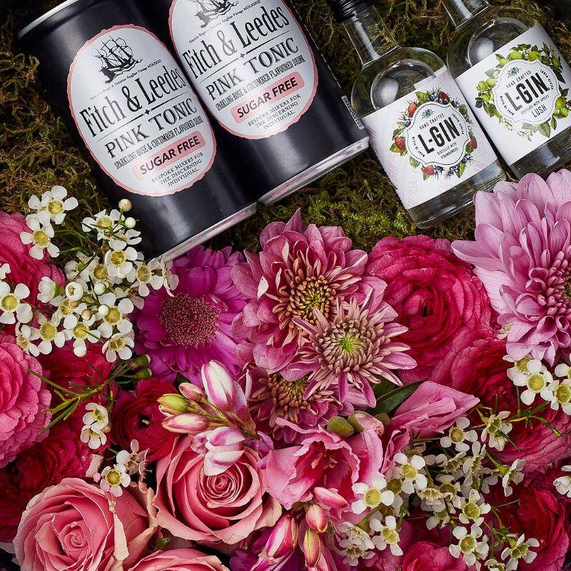 Close-up of pink flowers, L-Gin bottles, and Fitch & Leedes Pink Tonic, surrounded by fresh blooms