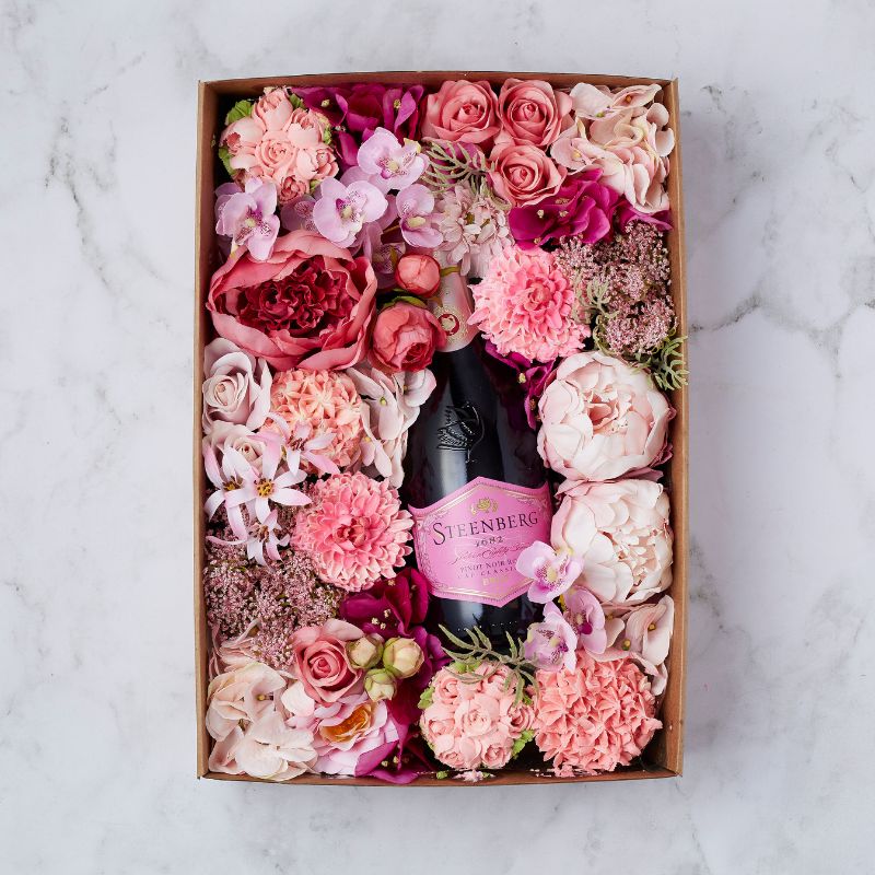 A beautifully arranged gift box featuring a bottle of Steenberg Pinot Noir Brut Rosé nestled among elegant pink and blush flowers.