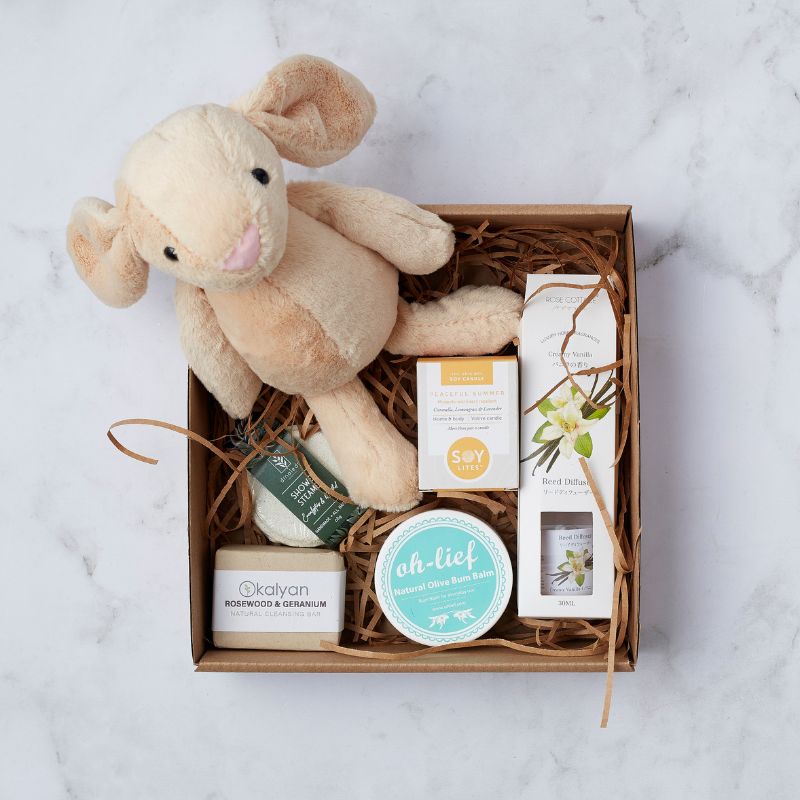 Gift box with plush toy, natural skincare items, soy candle, reed diffuser, and olive bum balm