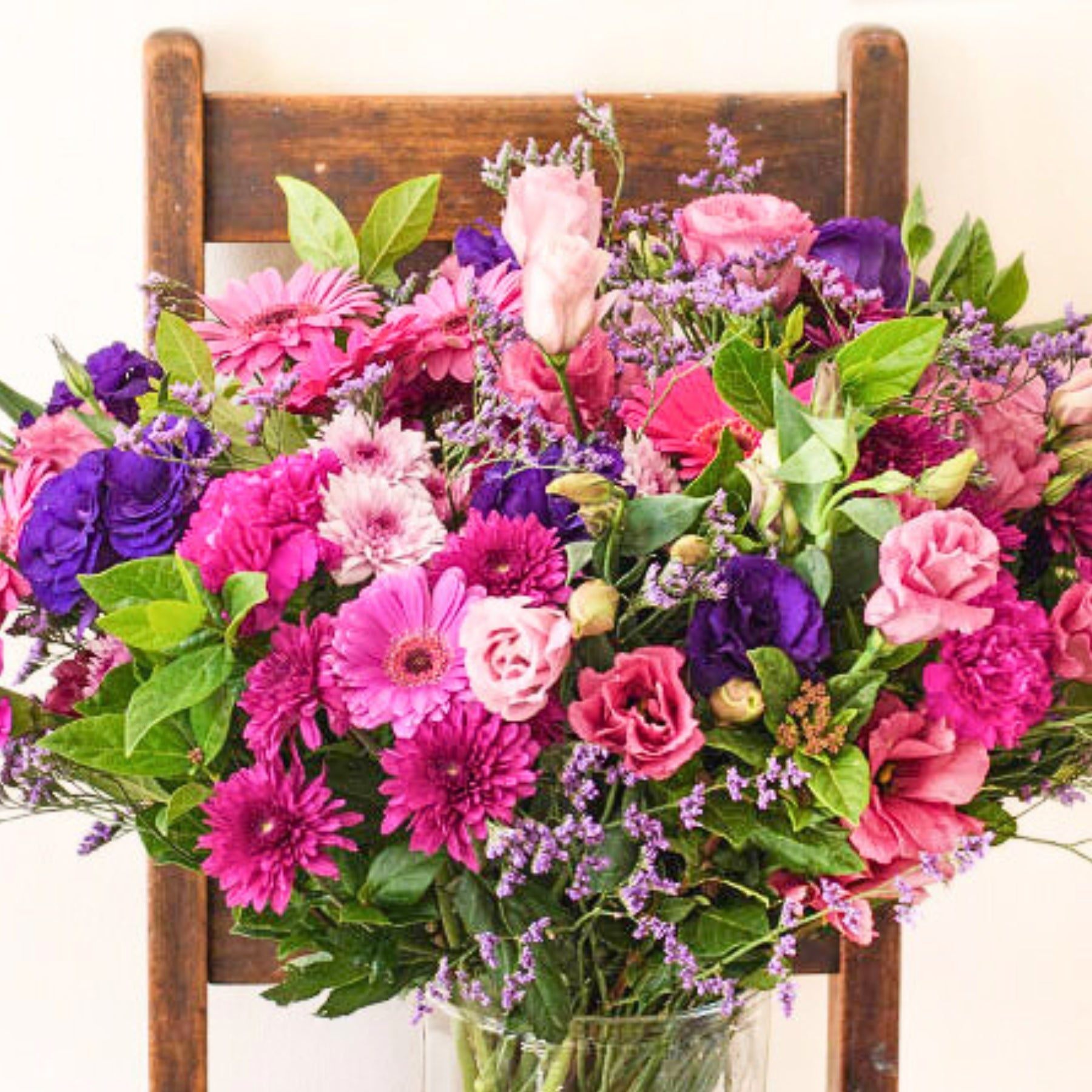 Vibrant bouquet of pink and purple flowers, beautifully arranged in a glass vase on a wooden chair.