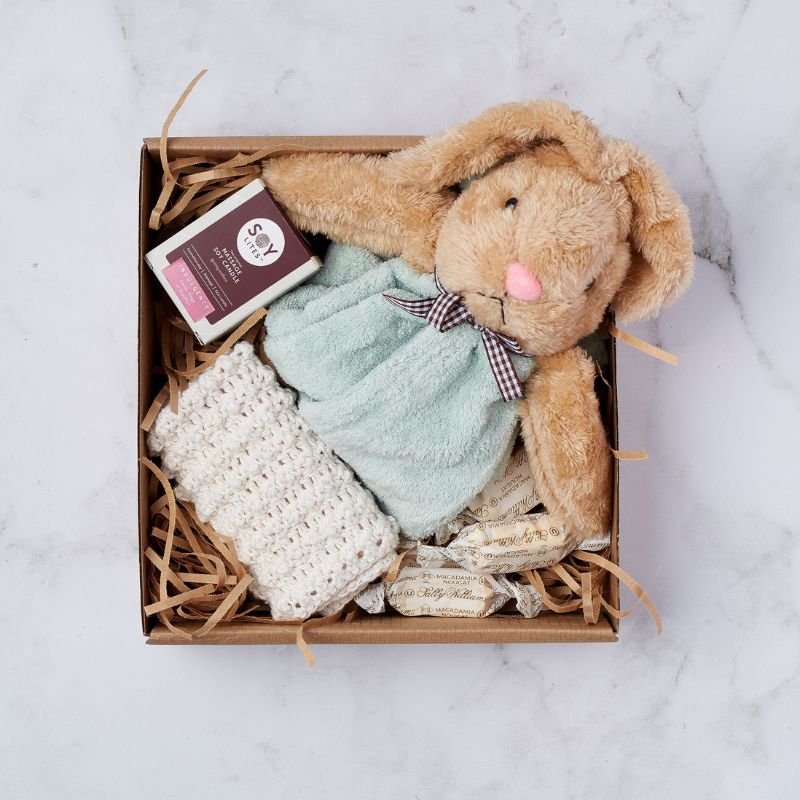 Gift box with a plush bunny, crocheted blanket, Soy Lites candle, and individually wrapped macadamia nougats.