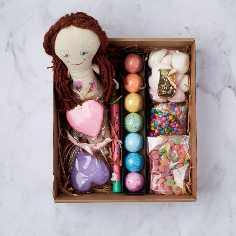 Kids gift box with a handmade doll, colourful bath bombs, heart-shaped cookies, musical flute, and assorted sweets.