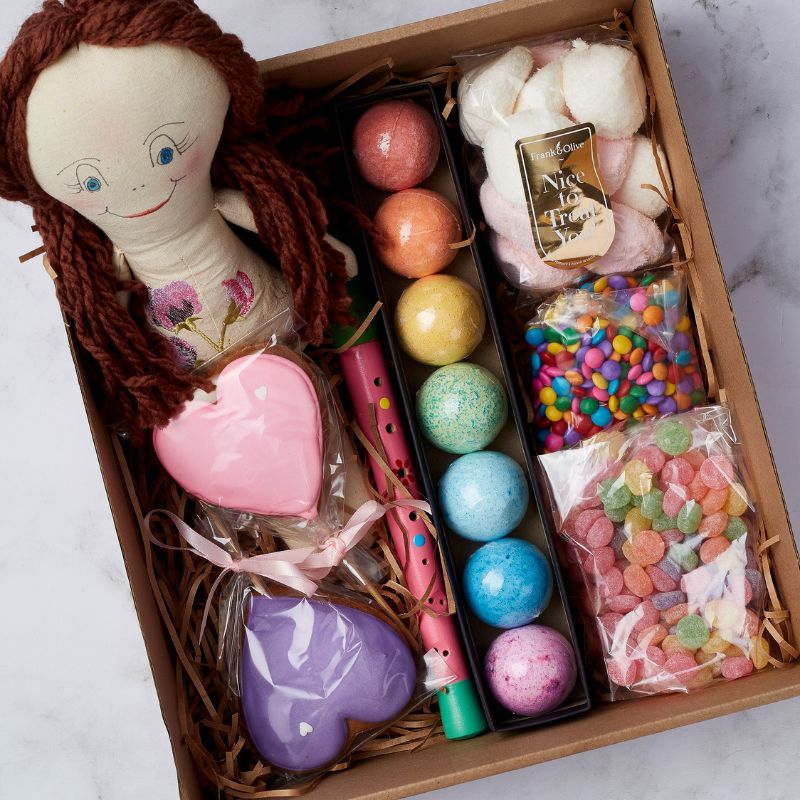 Children's gift set featuring a doll, heart-shaped cookies, bath bombs, candy assortment, and fun pink and green flute.