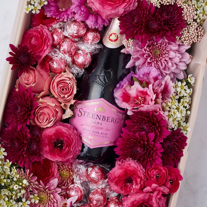 Close-up of a Steenberg rosé bottle surrounded by vibrant pink and red fresh flowers.