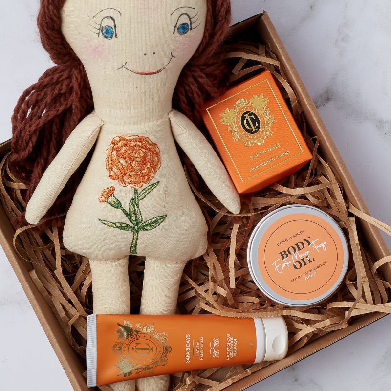 Gift box with handmade doll, body oil, hand cream, and scented candle arranged in eco-friendly packaging