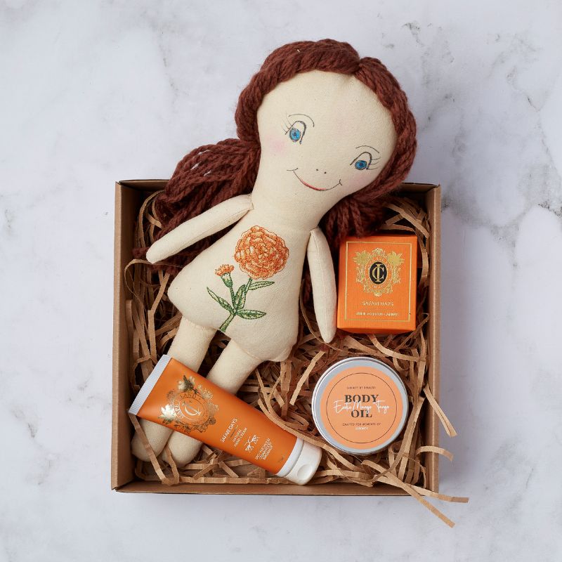 Handmade doll with floral embroidery alongside luxury body care products in a gift box