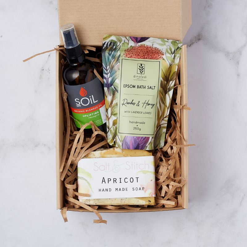 Gift box featuring Soil organic blended uplifting massage oil, rooibos and honey Epsom bath salt with lavender, and apricot handmade soap, nestled in shredded packing material.