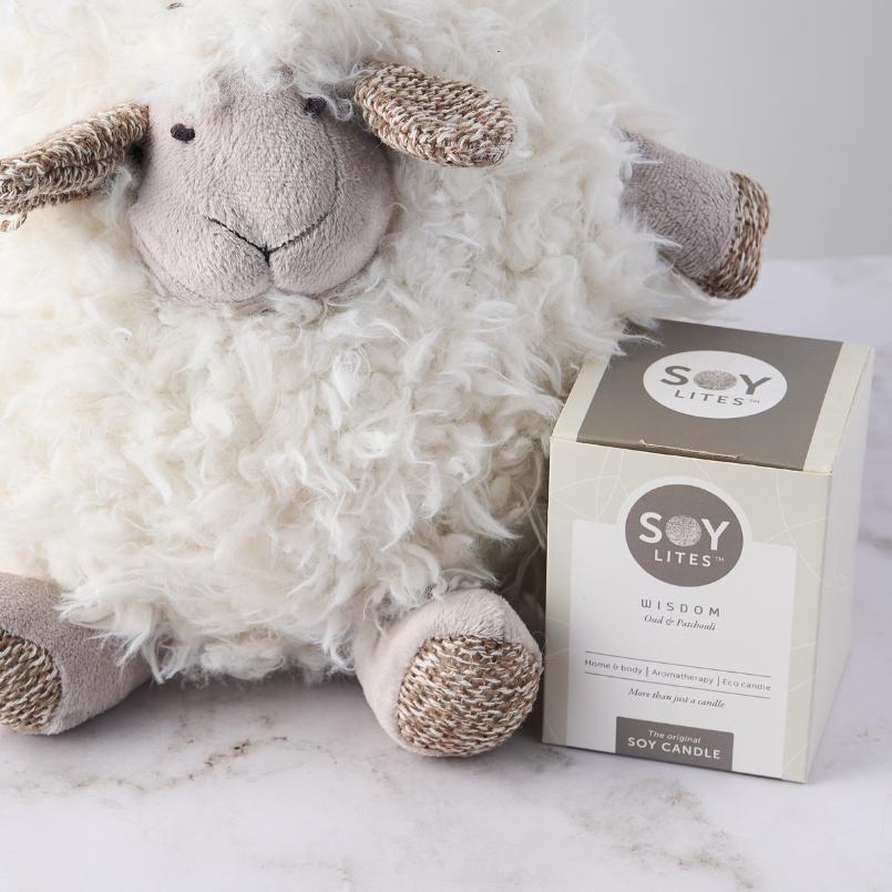 Close-up of the Shleep Time for Baby Girl Gift Set with a fluffy plush sheep and Soy Lites Wisdom candle on a white surface.