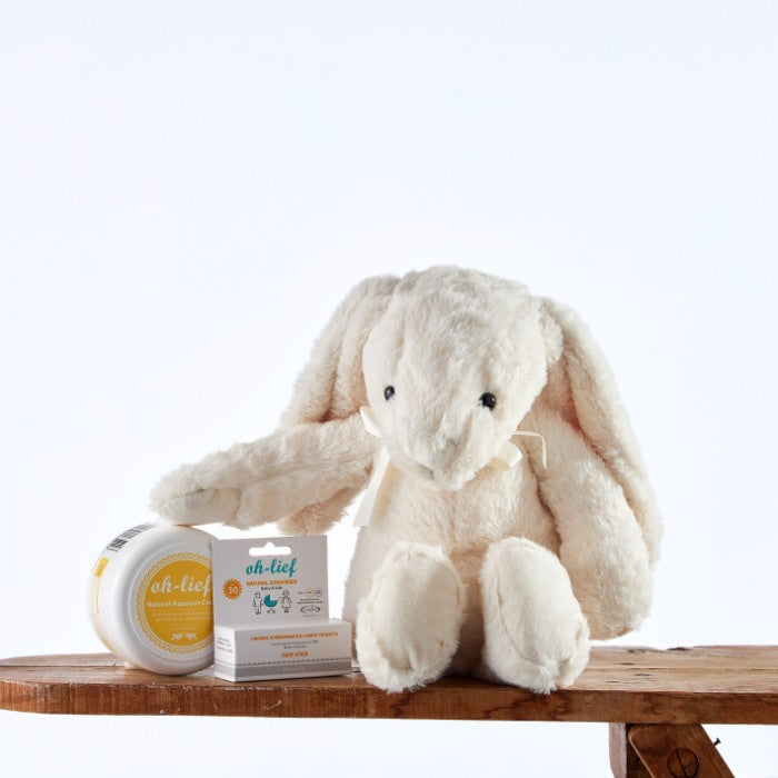 Snowy Snuggles Skincare Set featuring a white plush bunny next to natural skincare products including aqueous cream and zinc stick, presented on a wooden shelf.