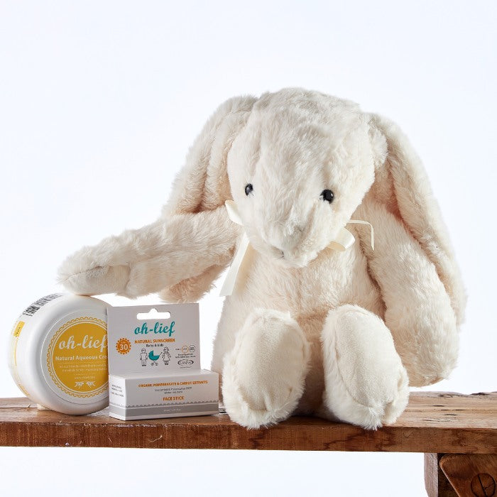 Close-up of the Snowy Snuggles Skincare Set with a soft white bunny toy and eco-friendly baby skin care products arranged on a rustic wooden surface.