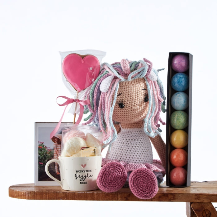 Sparkle & Shine Sweetheart Set features a handcrafted doll with colourful yarn hair, heart-shaped sweets, and a 'Worry Less Giggle More' mug on a wooden shelf.