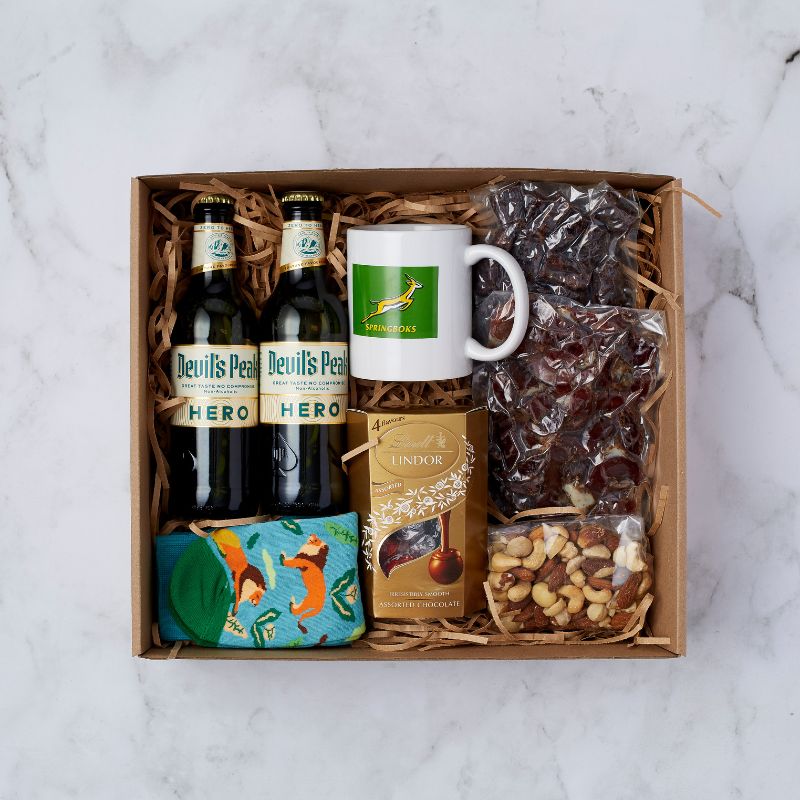 Gift box with two Devil's Peak Hero non-alcoholic beers, Springboks mug, Lindt chocolates, colourful socks, biltong, and mixed nuts.