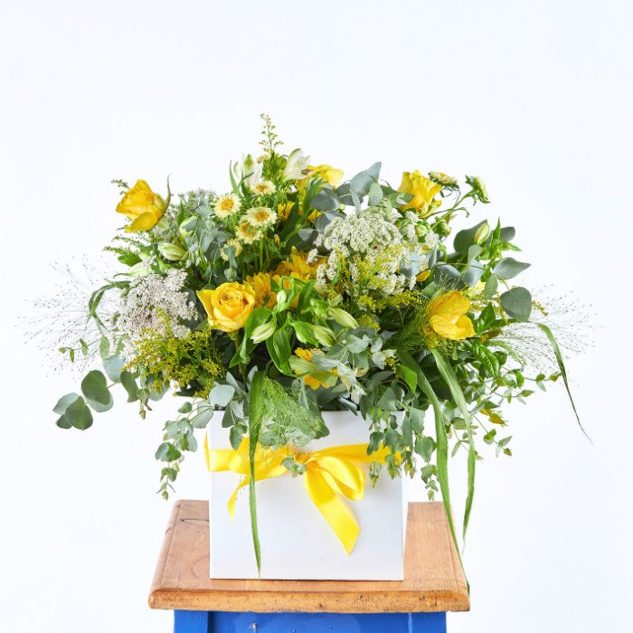 Sundance Bloom Box featuring a vibrant array of yellow roses and mixed wildflowers in a white box tied with a yellow ribbon.