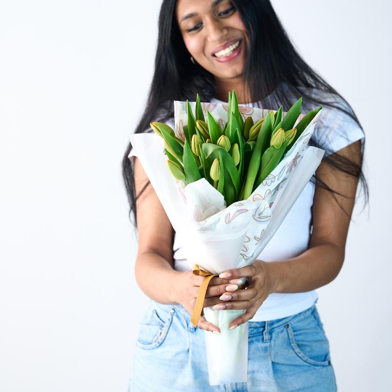 Woman holding a bouquet of yellow tulips wrapped in white floral paper, smiling gently.