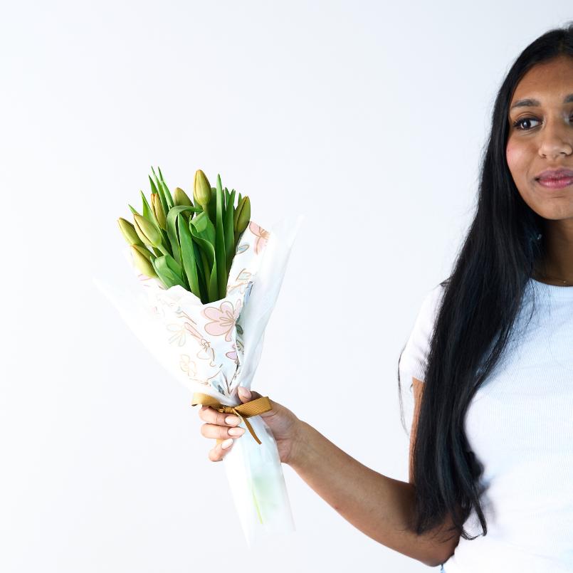 Close-up of a bouquet of yellow tulips wrapped in white floral paper, held by a woman in a white shirt.