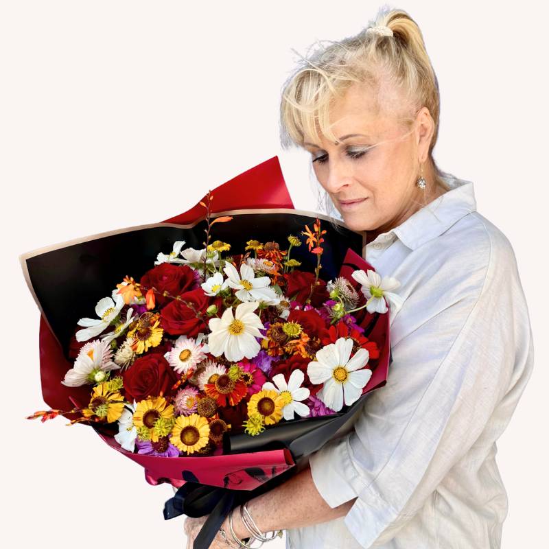 Wild Abundance bouquet with vibrant white cosmos, yellow daisies, and red roses, held by a serene individual - Fabulous Flowers & Gifts.