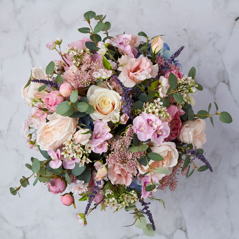 Top view of a luxurious silk flower arrangement showcasing soft pink roses, moody blue hydrangeas, and vibrant greenery.