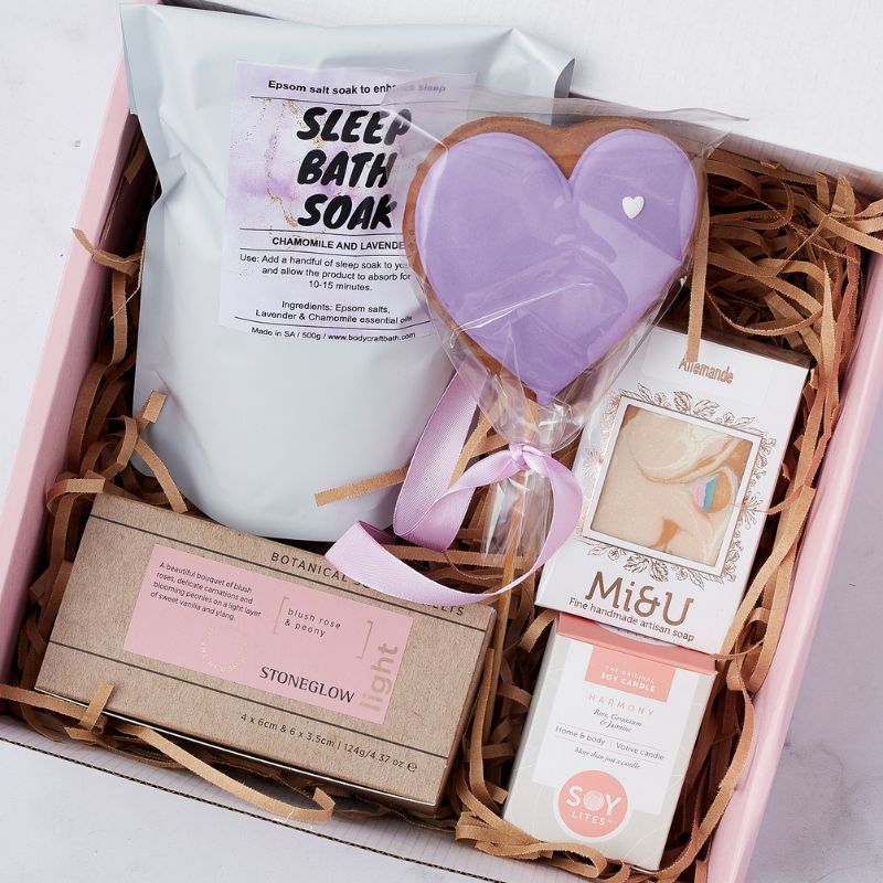 Pampering gift set including lavender chamomile bath soak, handmade soap, purple heart-shaped cookie, and scented candles.