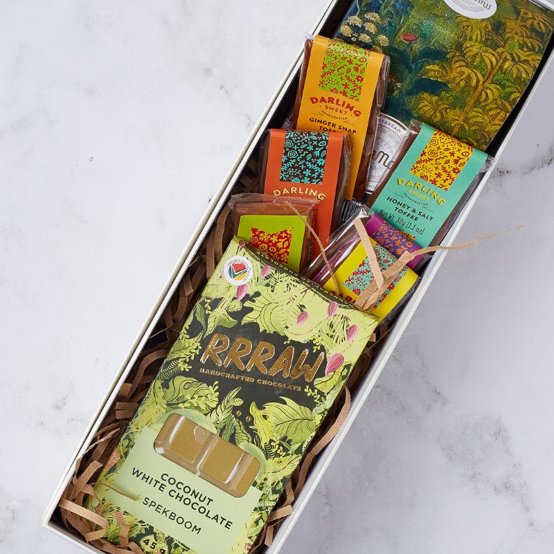 Close-up view of a gift box filled with Darling Sweet toffees, Rrraw coconut white chocolate bar, and other gourmet snacks arranged beautifully.