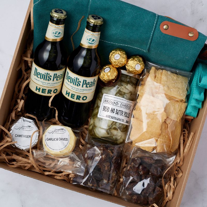 Close-up of Tasting Adventure Gift Box with Devil's Peak Hero non-alcoholic lagers, Ferrero Rocher chocolates, pickles, cheese selection, crackers, biltong bites, and canvas cooler bag.