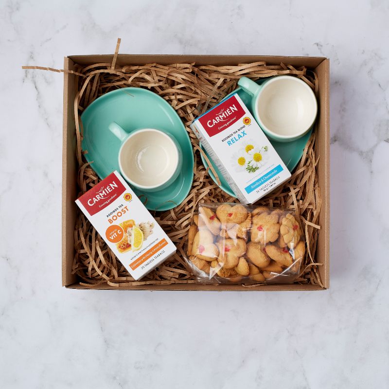 Gift box with two teal teacups, Carmién Rooibos tea boxes in Boost and Relax blends, and a pack of heart-shaped biscuits.