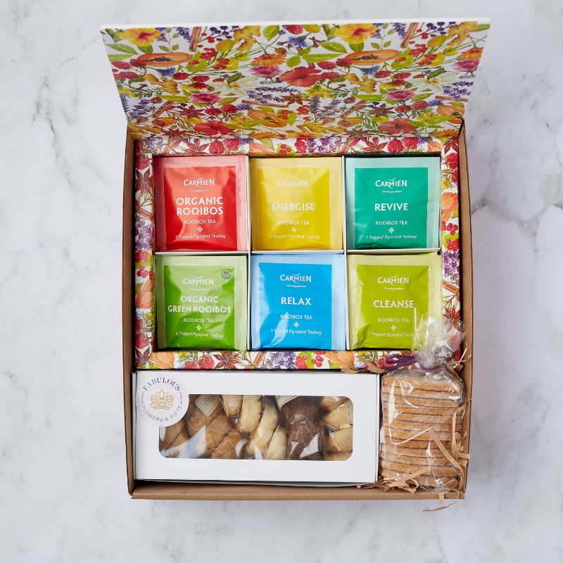 Top view of a beautifully presented Tea Treat Gift Box featuring six colourful Carmién organic rooibos tea flavours and an assortment of biscuits, carefully arranged in a vibrant floral box.