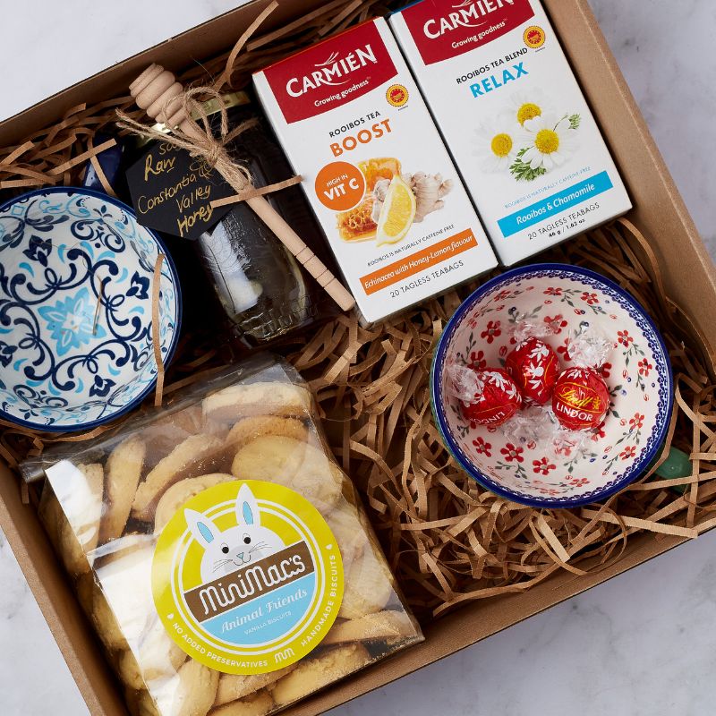 Tea gift set featuring rooibos tea, honey, ceramic bowls, biscuits, and chocolates